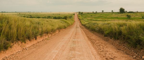 A dirt road running straight out through open fields to the horizon.