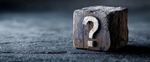 A weathered block of wood marked with a question mark.
